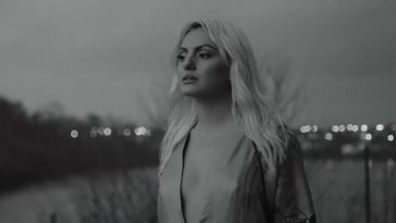 Still from the "Obsesii" music video which sees Alexandra Stan in a black and white filter wearing an open neck-line dress