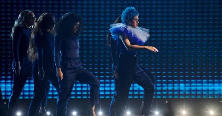 Eurovision 2020 Australia act Montaigne performing her song "Don't Break Me" on the Australia Decides stage, with blue curly short hair, taking inspiration from Pokémon's Mr. Mine