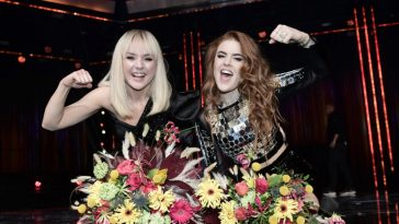 Winners of Melodifestivalen 2020, Anna Bergendahl and Dotter, celebrating their wins with raised arms and flowers on a table in front of them.
