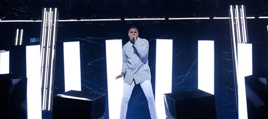 Mohombi in white jeans and a light blue jacket performing his song "Winners" on the Melodifestivalen 2020 stage.