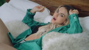A still from the "Man" music video with JoJo lying down on a bed, wearing an opened green shirt, a black bra, and grey underwear.