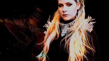 Avril Lavigne promo photo for her charity single "Warrior" wearing a silver neck armour piece with the background displaying a shadow of body armour.