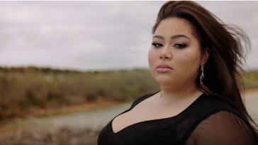 Still from the "All Of My Love" music video which sees Destiny standing on a beach in a black dress, staring at the camera as the wind whips her hair behind her.