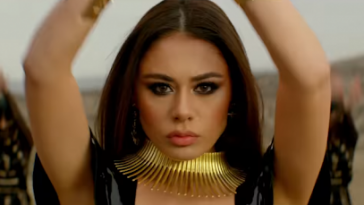 Still from the music video to "Cleopatra" which sees Efendi with her arms raised wearing a gold neck choker brace in the desert.