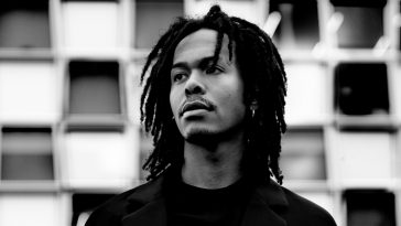 Black and white photo of Jeangu Macrooy in a press photo for "Grow" with his head turned and intermittent square wall design behind him.