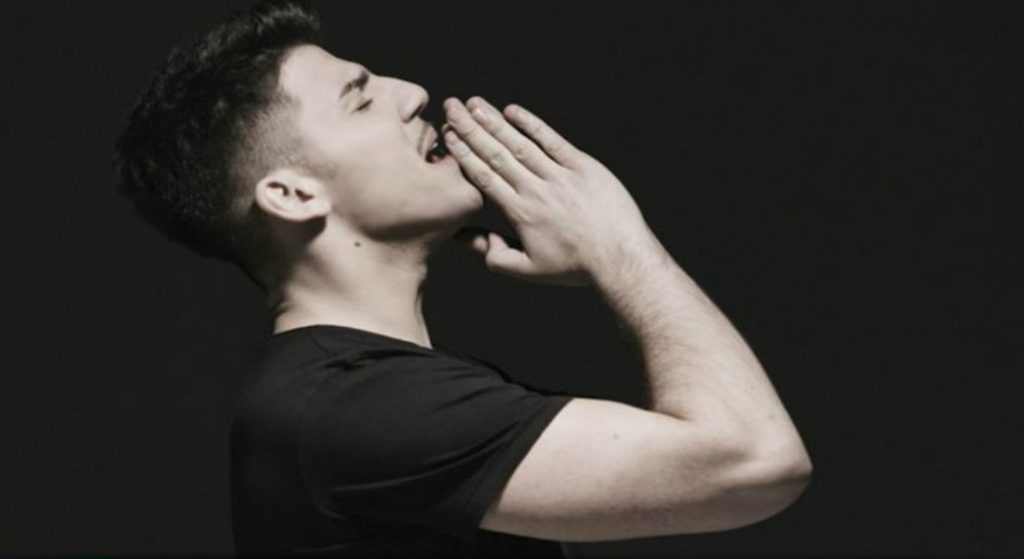 Cyprus' Eurovision 2020 act, Sandro, in his music video for the song "Running" turned to the side, wearing a black t-shirt, with his hands together, raised to his chin.