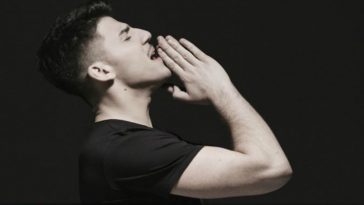 Cyprus' Eurovision 2020 act, Sandro, in his music video for the song "Running" turned to the side, wearing a black t-shirt, with his hands together, raised to his chin.