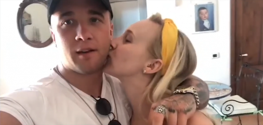 Still from "Something To Prove" music video where Sam Callahan is wearing a white t-shirt and a black cap, and his girlfriend, Robyn Hatton kisses his cheek.