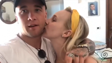 Still from "Something To Prove" music video where Sam Callahan is wearing a white t-shirt and a black cap, and his girlfriend, Robyn Hatton kisses his cheek.