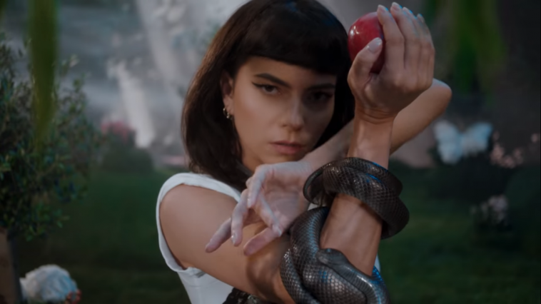 A still from the "Not My Baby" music video which sees INNA staring into the camera holding up a red apple with a black snake wrapped around her arm set within a garden.