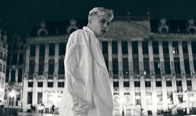 Loïc Nottet in the music video for "Mr/Mme" wearing a white oversized shirt looking off to the right located in Brussels.