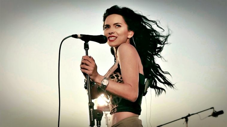INNA singing on stage into a microphone with the wind whipping her hair behind her.