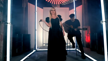 Alexandra Stan performing in the video for "Take Me Home" with Mircea Steriu behind playing the guitar.