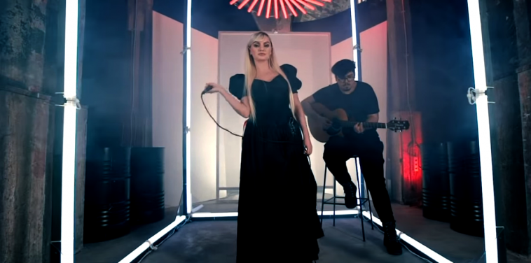 Alexandra Stan performing in the video for "Take Me Home" with Mircea Steriu behind playing the guitar.