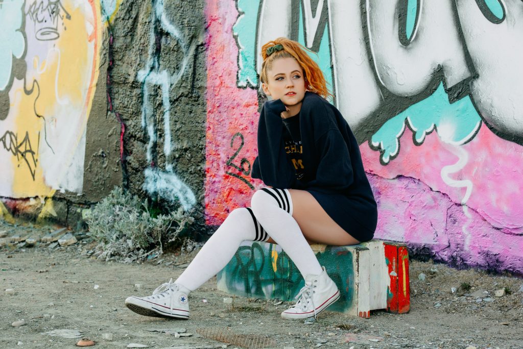 Interview promo picture which sees Janet Devlin in a black jumper and knee-high socks sitting on a concrete block.