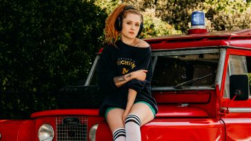 Janet Devlin promo shot for interview, she is on the bonnet of a red truck, wearing a black jumper and some headphones, and knee-high socks.