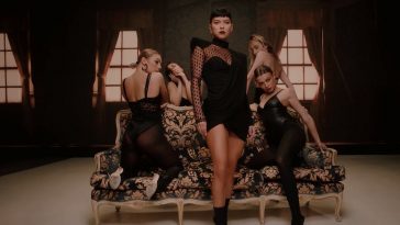 Music video still from "VKTM" by SICKOTOY, INNA & TAG, which sees INNA standing infront of a sofa with four backing dancers, all dressed in black provocative clothes.