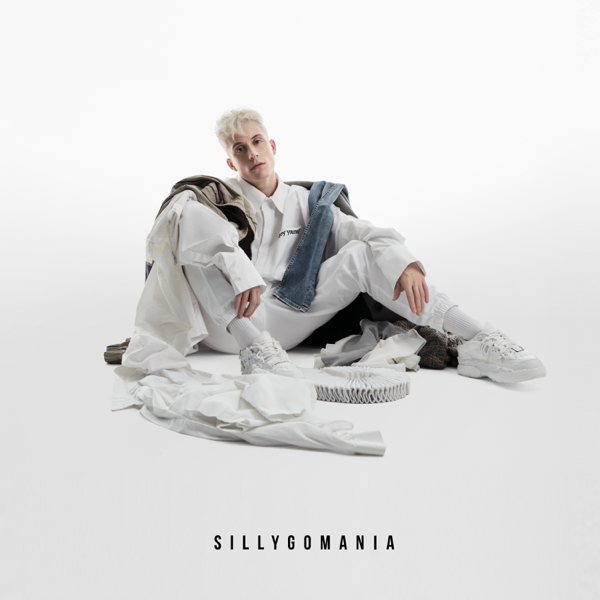 Album artwork for Sillygomania which sees Loïc Nottet sitting with his knees up and his arms on top of his legs, dressed in white with white clothes strewn around him of different colours with a white background.