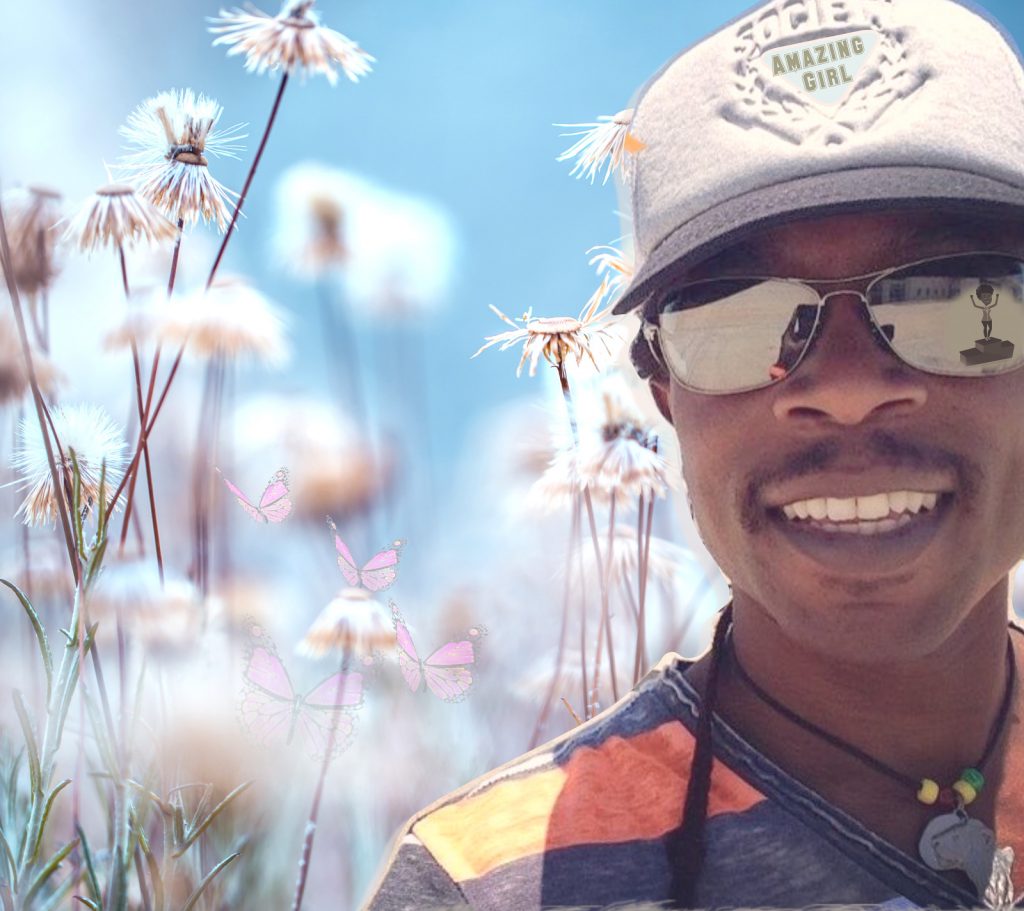 JayQ The Legend wearing a snow-white cap with the title of the song emblazoned on the front. He's also wearing a dark grey and orange striped t-shirt and there's a field of dandelions behind him.