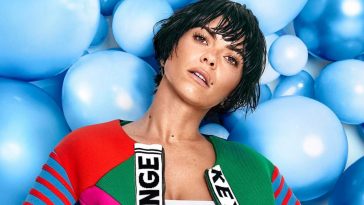 Press photo of INNA wearing a white top under a multi-coloured jacket and her short-hair wet.