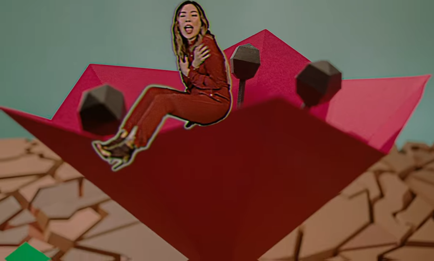 Still from the "Paper Dragon" music video which sees Dami Im in a red jumpsuit displayed as a paper sticker whilst sitting on a paper rose in the desert.