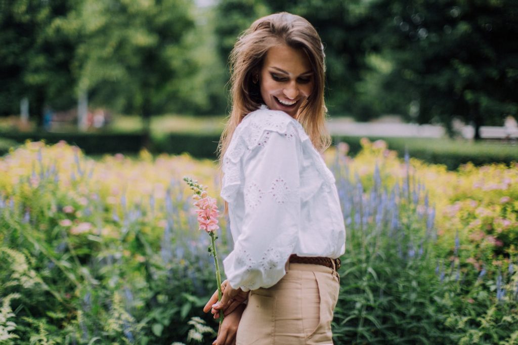 woman in white long sleeve shirt and brown pants holding flower