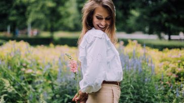woman in white long sleeve shirt and brown pants holding flower