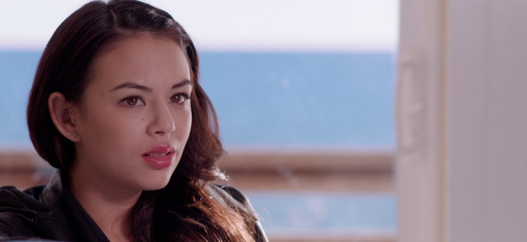 Image from Until We Meet Again, Janel PArrish is looking towards the the camera with a blue sea in the background.