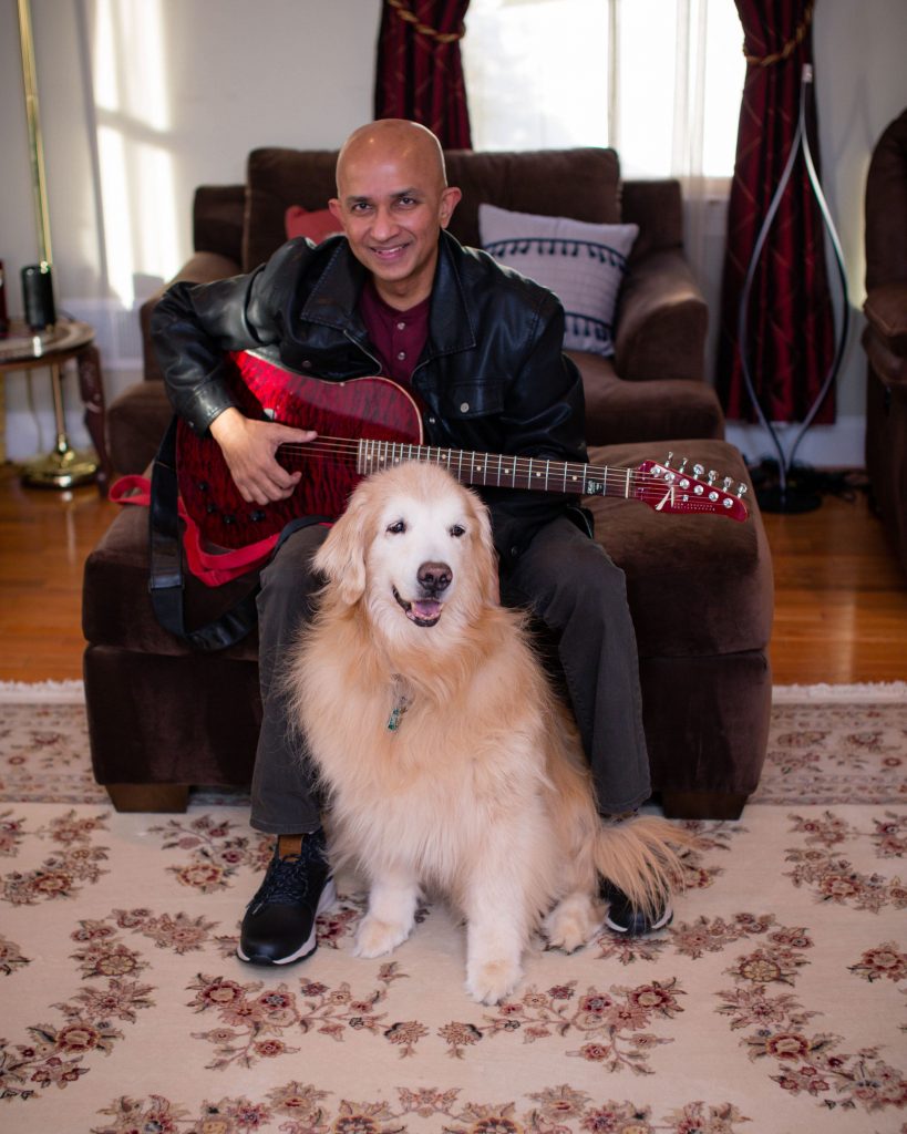Jacob Chacko sits down on a chair holding a guitar with his white dog sitting in front of him for promotion of "Good Moment".