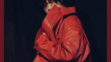 Castle KYD poses at the camera, looking over his shoulder while wearing a massively over-sized bright-red coat, in a press image for "Melatonin"