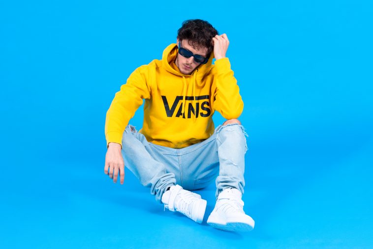 Scott the Pisces in a promotional image for "Summer '22" which sees him wearing a bright yellow Vans hoodie, light blue jeans, and white hi-top trainers, with a bright blue background.