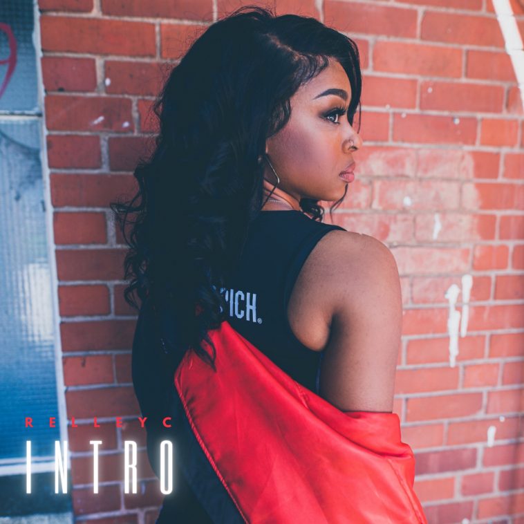 Single artwork for "Intro" which sees Relley C against a brick wall looking over her shoulder as her black back-length hair is over the other shoulder, she's wearing a black vest top and has a red coat draped over her arms and across her back.