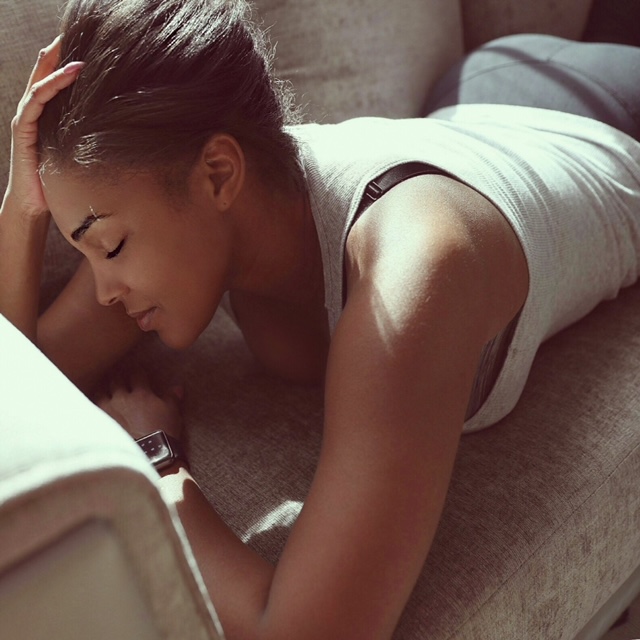 Promotional photo for "Keep a Smile" by OnnaDi which sees her lying face down on a cream coloured couch, resting on her arms, wearing a white tank top with her hand in her tied-back hair.