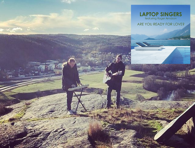 Laptop Singers perform on top of a hill with a beautiful landscape behind them, dressed in warm coats as it's clearly cold, with the single cover artwork for "Are You Ready For Love?" displayed in the top right corner.