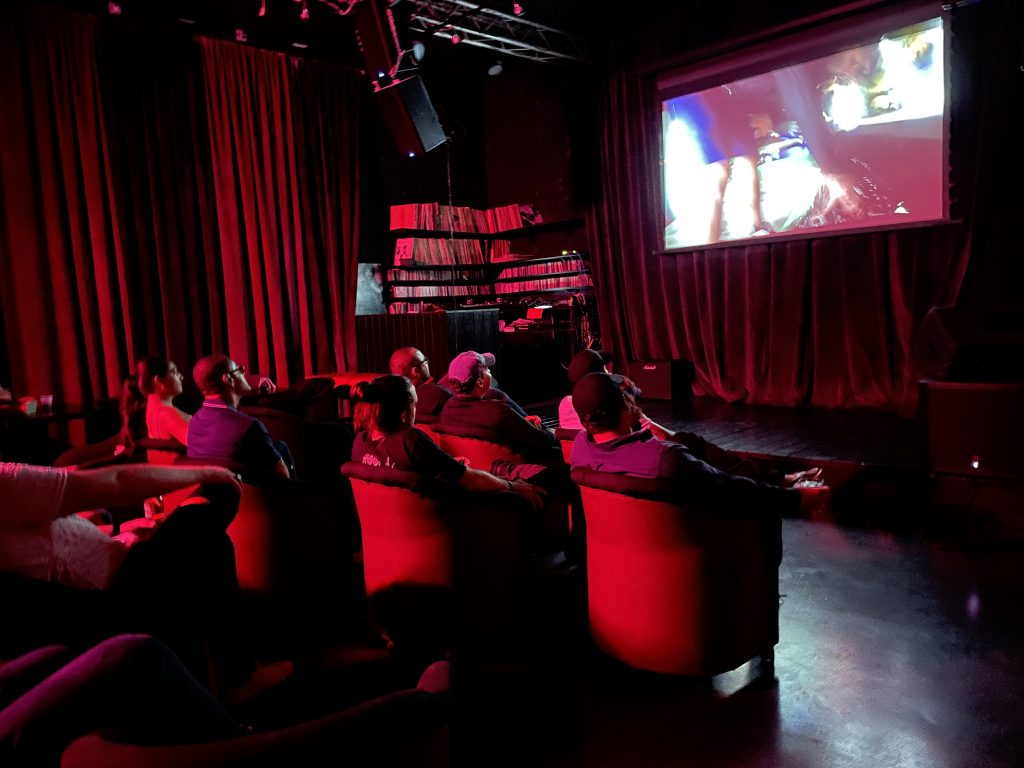 A crowd looking at a display screen all illuminated by a red light.