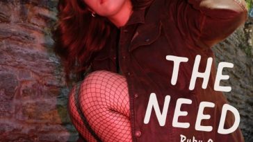 Album cover artwork for "The Need" by Ruby Sue which sees her crouching with her right body against a brick wall, ,with her red coat on but still looking very xovers