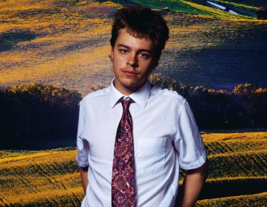 Promotional photo for "Superstar" which sees Christian Leave wearing a white shirt and a patterned light-red tie, backed by a countryside landscape.