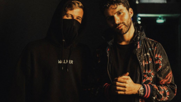 Promotional image for Alan Walker's remix of "All Around the World (La La La)" by R3HAB & A Touch of Class. Alan Walker and R3HAB are standing next to each other in a dark, dank warehouse, with Alan Walker wearing a black hoodie with the hood up and he is wearing a mask, so you can only see a bit of his hair, his forehead and his eyes. R3HAB is standing next to him, wearing an orange-black bomber jacket over a black t-shirt and he has his left arm out in front of him, He's looking at the camera and now has dark brown hair with a long stubble beard.