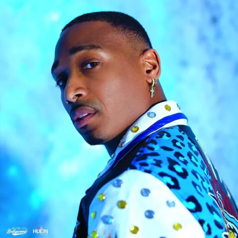Promotional picture for "Grandma House" which sees a head shot of J Young MDK looking over his shoulder. The background is a faded sky blue, whilst he is wearing a deeper blue leopard-print jacket with white sleeves and collar that have blue and yellow gem stones on. He has short black hair and a diamond cross hanging from a gold and diamond loop earring.
