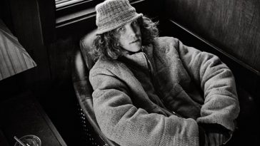 Promotional photo for "Bad Radio" which is a black and white photograph of Felly relaxing in an armchair with a big oversize coat on and a hat over his curly hair.