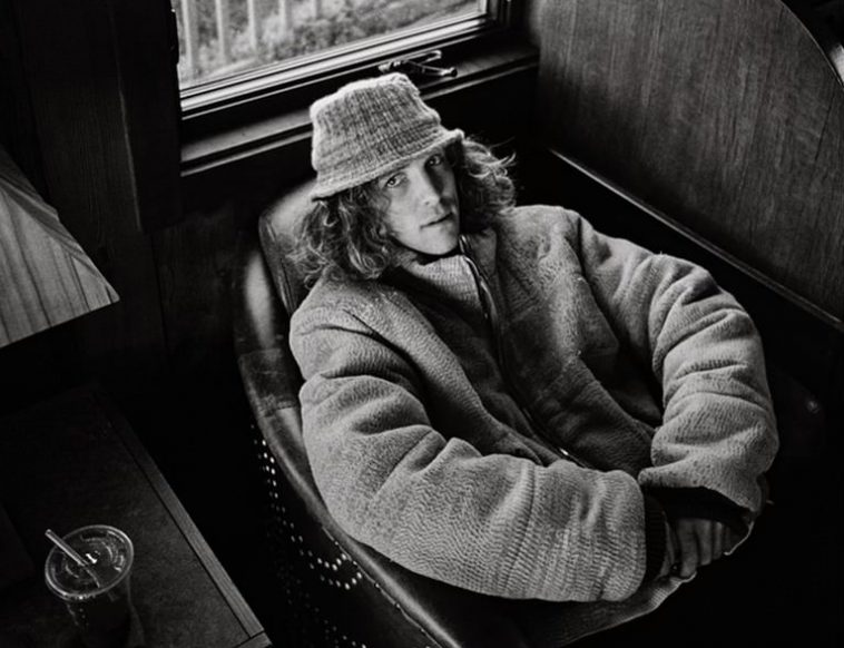 Promotional photo for "Bad Radio" which is a black and white photograph of Felly relaxing in an armchair with a big oversize coat on and a hat over his curly hair.