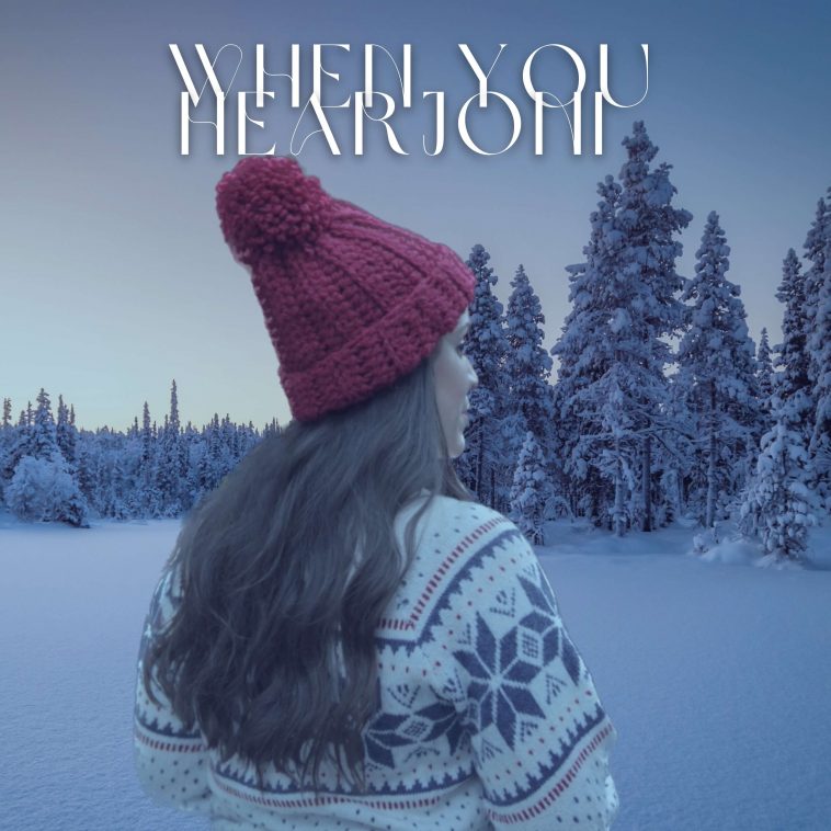 Single cover artwork for "When You Hear Joni", which sees Gina Naomi Baez in a snowy field looking at a few trees in the near distance. She's wearing a red beanie hat with her long brown hair down her back and a white jumper with blue snowflakes patterned on it. She's facing away from the camera.