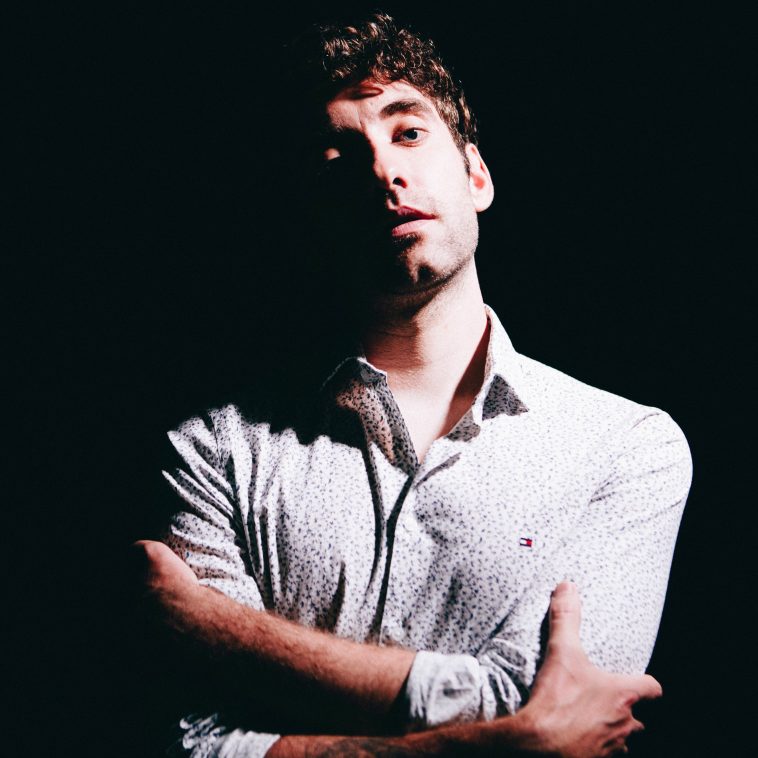 Promotional photo for "I Wish I Was Flawless, I'm Not" EP which sees BANNERS standing in front of a black backdrop, wearing a white long-sleeved shirt with the sleeves rolled up to his mid-lower arm. His arms are crossed and he has his head slightly tilted to the side.