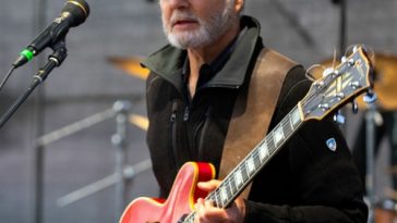 Singer-songwriter of "Emotionality", Dan Zalles performing on-stage with a red guitar and a beige trucker cap.