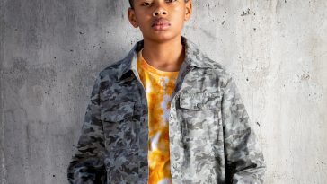 Phoenix Nicholson at 11 years old standing in front of a grey background wearing a dark grey and white tie-dye denim jacket over an orange and white tie-dye t-shirt.