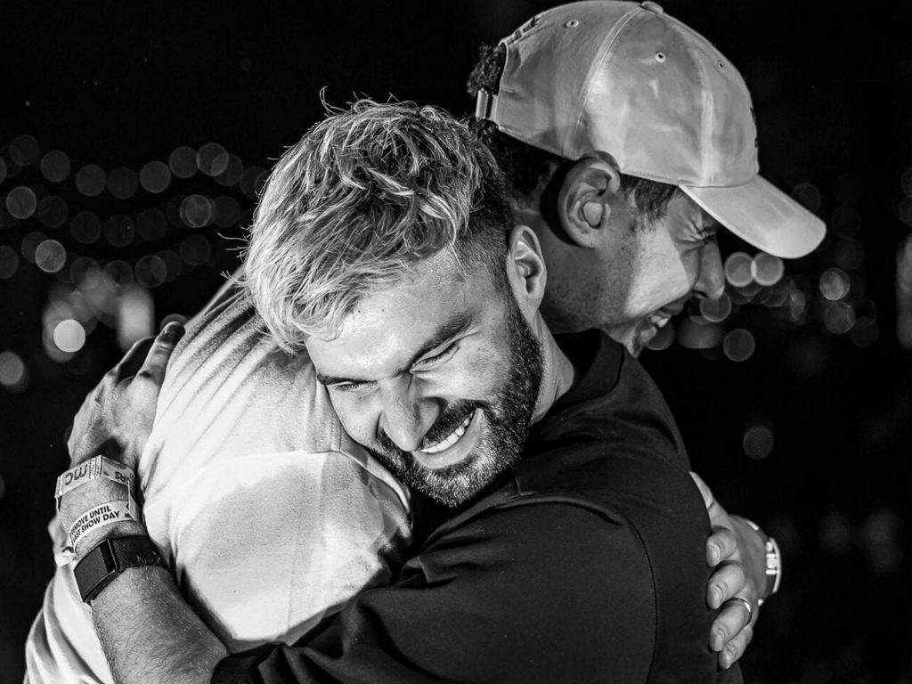 Black and white promotional photo for "Shockwave" which sees Afrojack wearing a flat cap embracing R3HAB in a friendship hug, with R3HAB grinning with a huge smile.