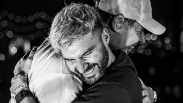 Black and white promotional photo for "Shockwave" which sees Afrojack wearing a flat cap embracing R3HAB in a friendship hug, with R3HAB grinning with a huge smile.