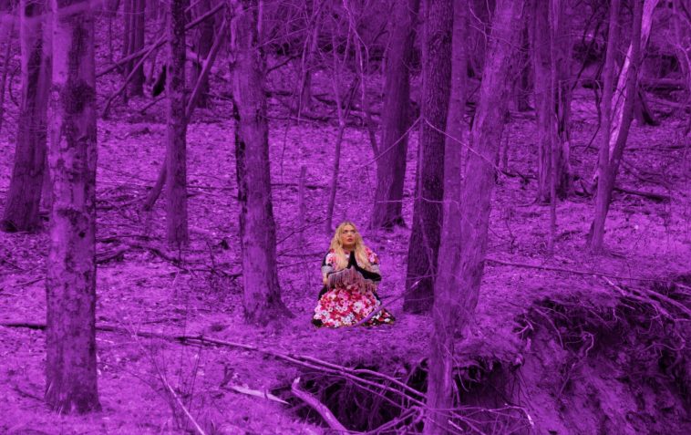 Promotional photo for the Initial Talk remix of "Long Way" which sees Chayla Hope sitting crossed-legged in a forest with her hands together in a prayer. The forest is filtered to a neon purple, while Chayla is sitting with her white and red dress and black gloves, praying.