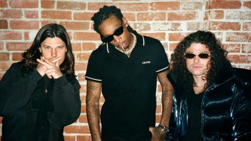 Promotional photo for "Sh Sh Sh (Hit That)" which sees DVBBS posing with Wiz Khalifa against a bright wall, with the rapper in the middle. All three are wearing black, with Wiz Khalifa and one-half of DVBBS donning shades.