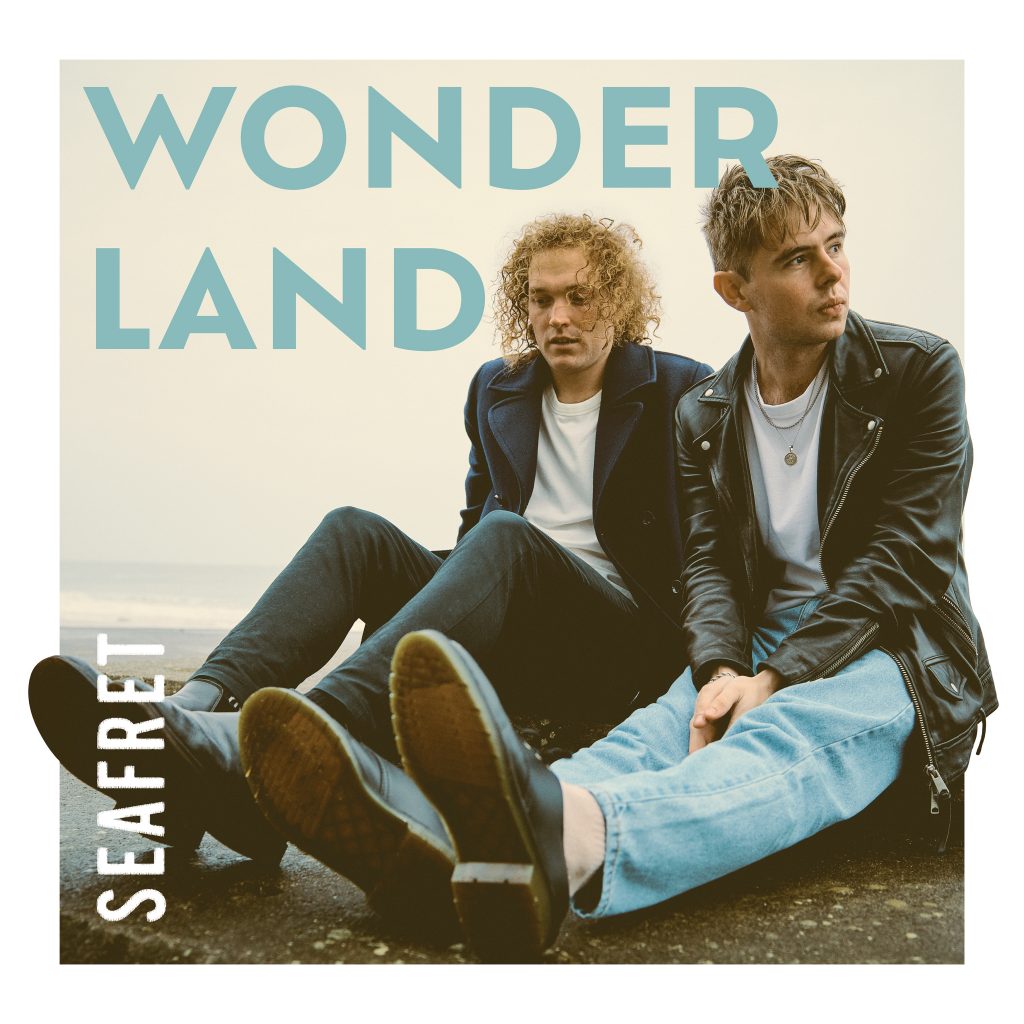 Official album artwork for "Wonderland" which will contain the track "Remind Me to Forget You", which sees Seafret sitting on the beach with their legs out in front of them, and it's a cold and wet day but the duo are relaxing even though their clearly cold with their black jackets on and their hair is wet.